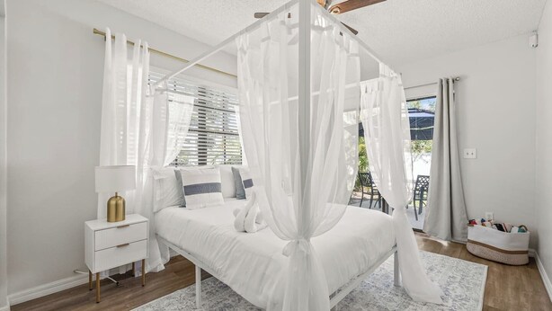 A bedroom with a canopy bed, a bedside table, a lamp, and a view of the outdoors. - 4BR Oasis | Jacuzzi/Gym & Game room | Sleeps 12! (Tampa)