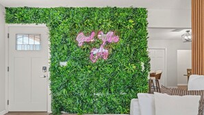 A living room with a green wall covered in plants, a white sofa, and a neon sign that reads "Good Vibes." - 4BR Oasis | Jacuzzi/Gym & Game room | Sleeps 12! (Tampa)