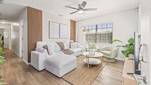 A modern living room with a white sofa, a coffee table, and a TV. - 4BR Oasis | Jacuzzi/Gym & Game room | Sleeps 12! (Tampa)