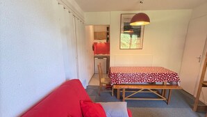 A compact living space with a red sofa, a wooden bench, and a dining table with a patterned tablecloth.