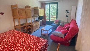 A compact room with bunk beds, a sofa, a table, and a window with a view of greenery.