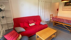 A red sofa with cushions, a grey armchair, a wooden coffee table, and a dining table with a patterned tablecloth.