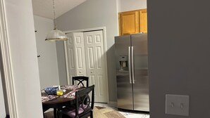 A kitchen with a stainless steel refrigerator, a wooden cabinet, and a dining area with a table and chairs.
