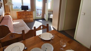 A cozy hotel room with a bed, a wooden dresser, a dining table set for two, and a television. - Avoriaz - Apartment 4 people, balcony, wifi (Avoriaz)