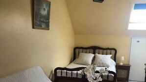 A bedroom with a bed, a bedside table with a lamp, a round glass table with a flower vase, and a painting on the wall. - Marjolaine Bed and Breakfast for 2 to 4 guests (Lourdes)