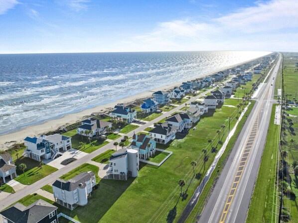 A coastal residential area with houses aligned along a road, a beach, and the ocean.