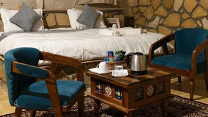 A bedroom with a bed, two chairs, a coffee table, and a stone wall. - Desert Island Camp & Resort Jaisalmer (Jaisalmer)