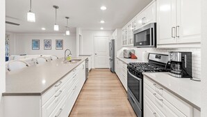 A modern kitchen with white cabinetry, a central island, stainless steel appliances, pendant lighting, and a tiled backsplash. - Walk to dinner, near Universal, EV charger, baby/pet gear included, fenced yard (Frisco)