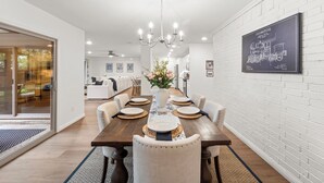 A dining area with a wooden table, white chairs, and a chandelier. - Walk to dinner, near Universal, EV charger, baby/pet gear included, fenced yard (Frisco)