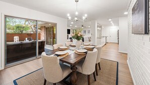 A dining area with a wooden table, chairs, a chandelier, and a view through glass doors. - Walk to dinner, near Universal, EV charger, baby/pet gear included, fenced yard (Frisco)