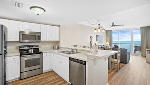 A modern kitchen with stainless steel appliances, a dishwasher, and a dining area with a view of the ocean. - Majestic Beach Towers 1-1903 (Panama City Beach)