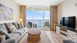 A living room with a sofa, chairs, a TV, and a balcony with a view of the sea. - Majestic Beach Towers 1-1903 (Panama City Beach)
