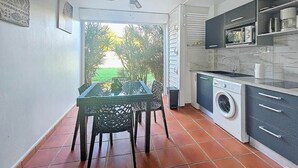Une cuisine compacte équipée d’un lave-linge, d’une table à manger avec des chaises, et offrant une vue sur la verdure environnante.