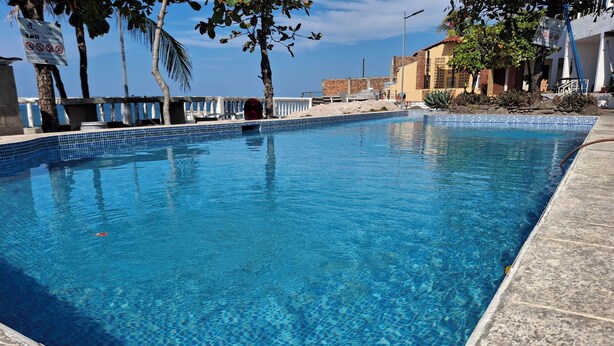 A clear blue pool with tiled edges, surrounded by palm trees and a building with a tiled roof.