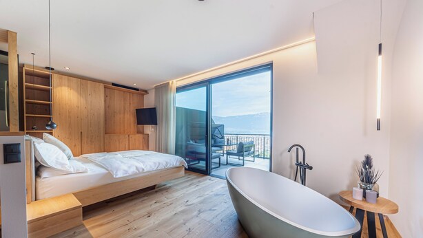 Una camera da letto moderna con un letto grande, una vasca da bagno indipendente e un balcone con vista.