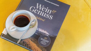 Un libro dal titolo "Wein & Genuss" con un cucchiaio e una tazza di caffè su una superficie gialla.