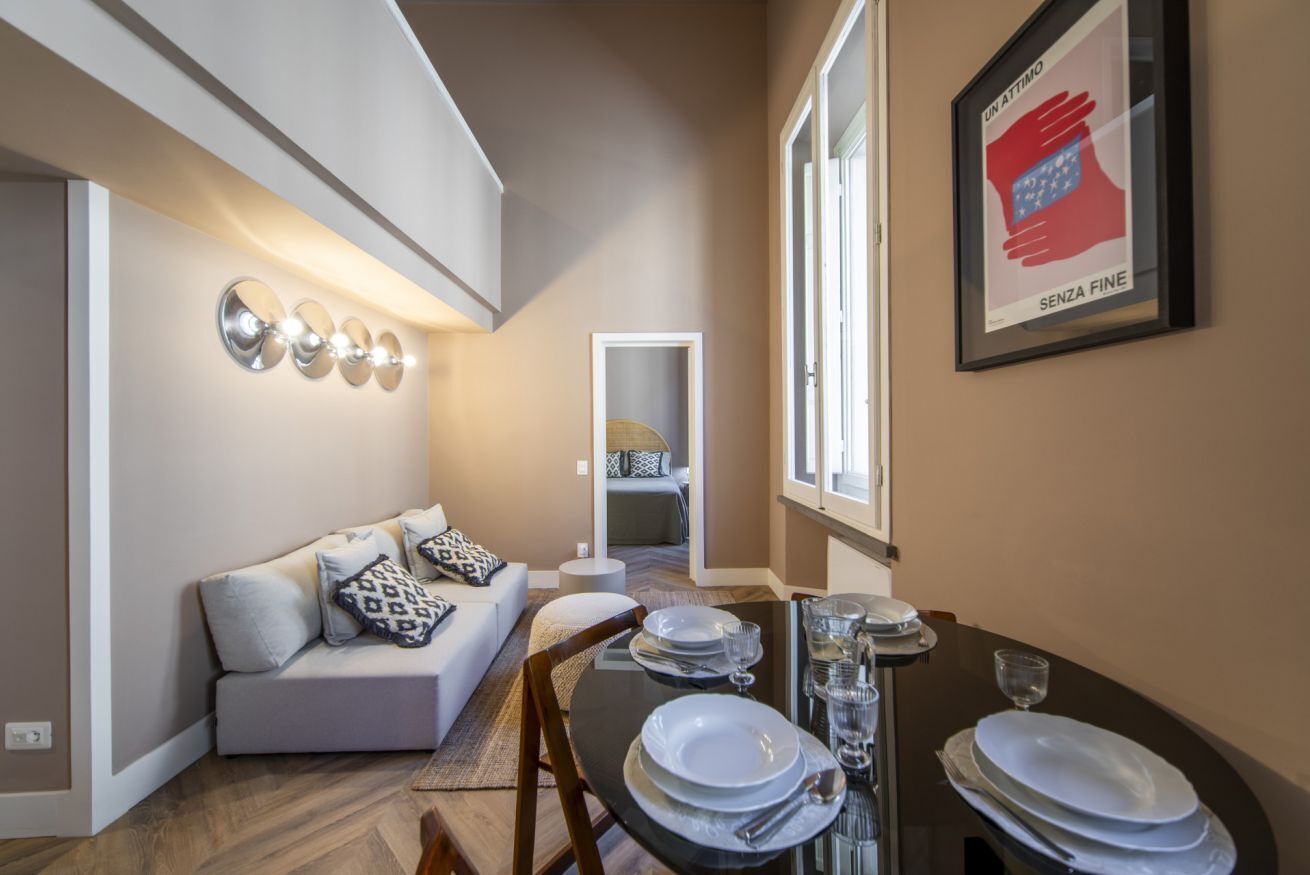 Uma sala de estar moderna com um sofá, uma mesa de jantar para quatro pessoas e um quadro na parede.
