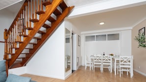 Et moderne interiør med en trætrappe, et spiseområde med hvide møbler og en grå sofa.