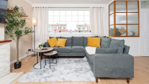 En moderne stue med en grå modulsofa, et lille rundt bord, en blød måtte og en potteplante.