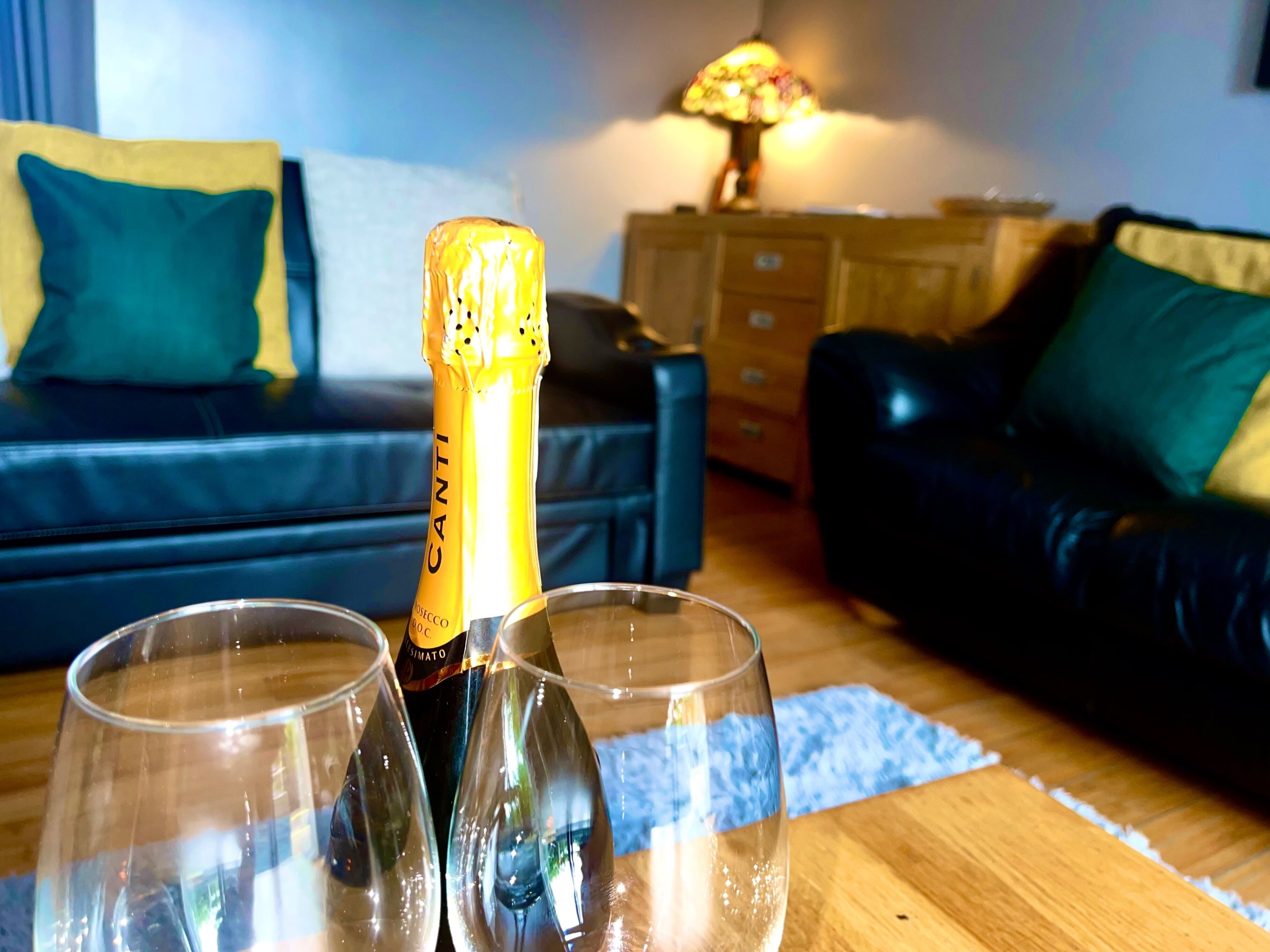 A bottle of Canti champagne and two glasses on a wooden table in a living room.