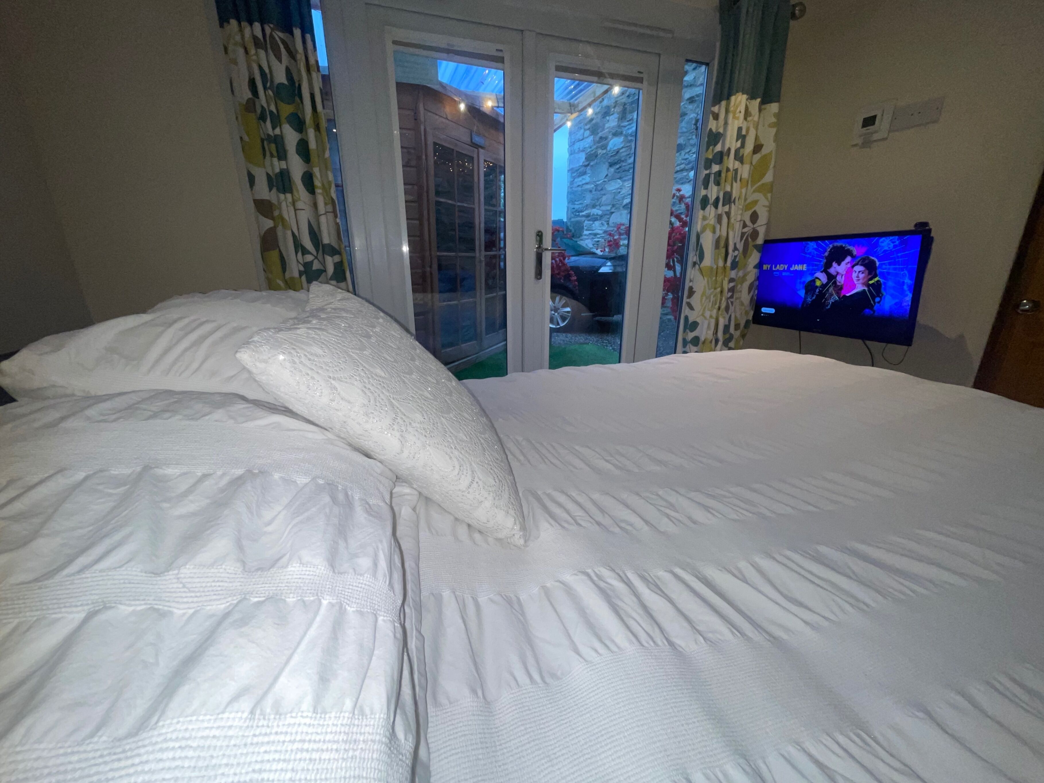 Quarto com uma cama grande, televisão na parede e porta de vidro deslizante para área externa.