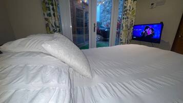 Quarto com uma cama grande, televisão na parede e porta de vidro deslizante para área externa.