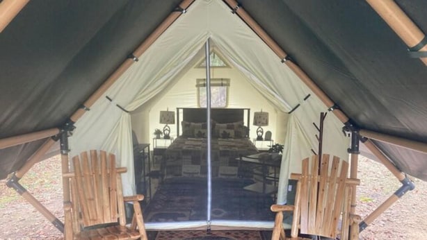 A tent with a central bed and two wooden chairs facing the bed. - The Water’s Edge Glamping Tent (Fort Payne)