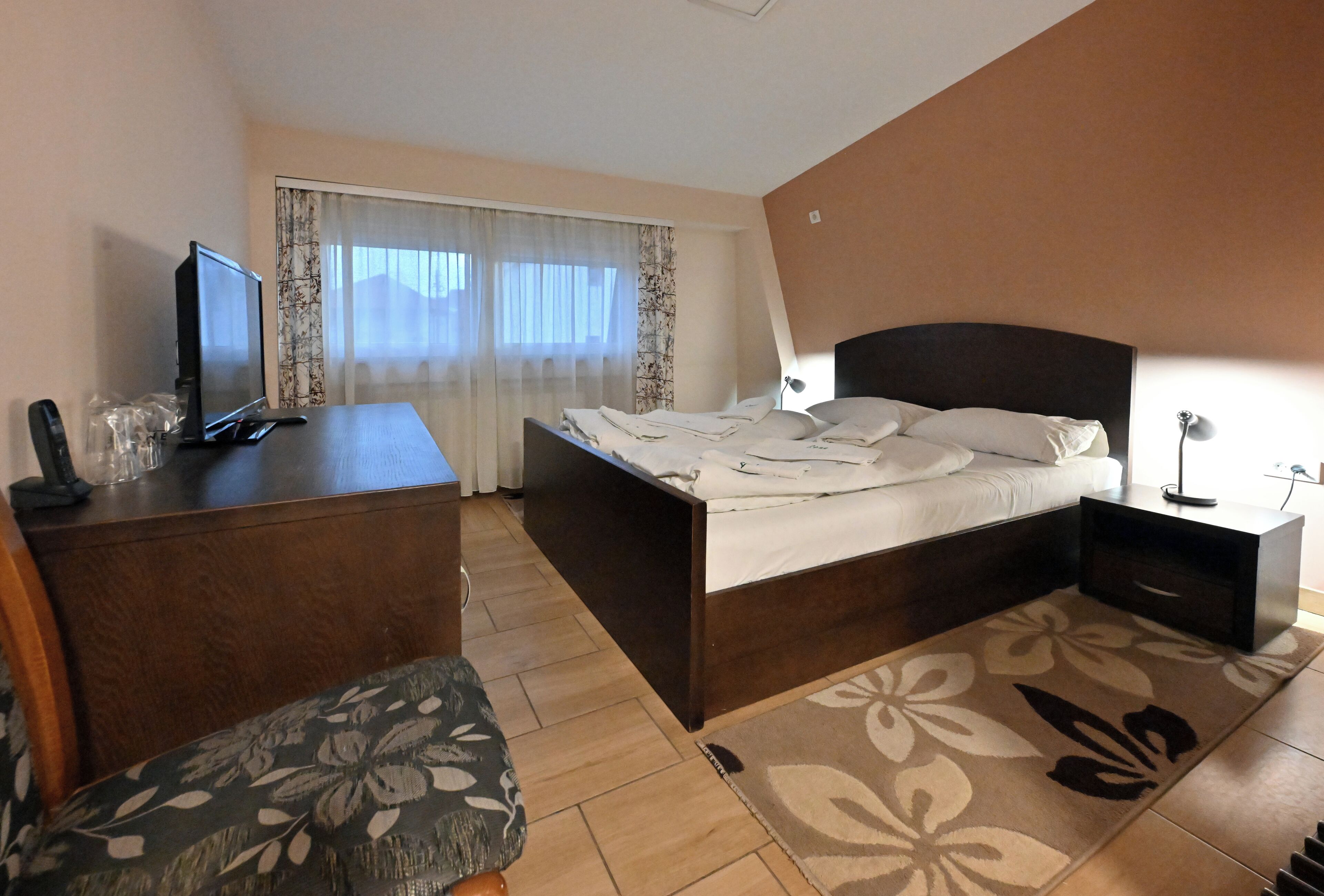 Un dormitorio con cama, escritorio, silla, televisor y ventana con cortinas.