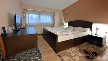 Un dormitorio con cama, escritorio, silla, televisor y ventana con cortinas.