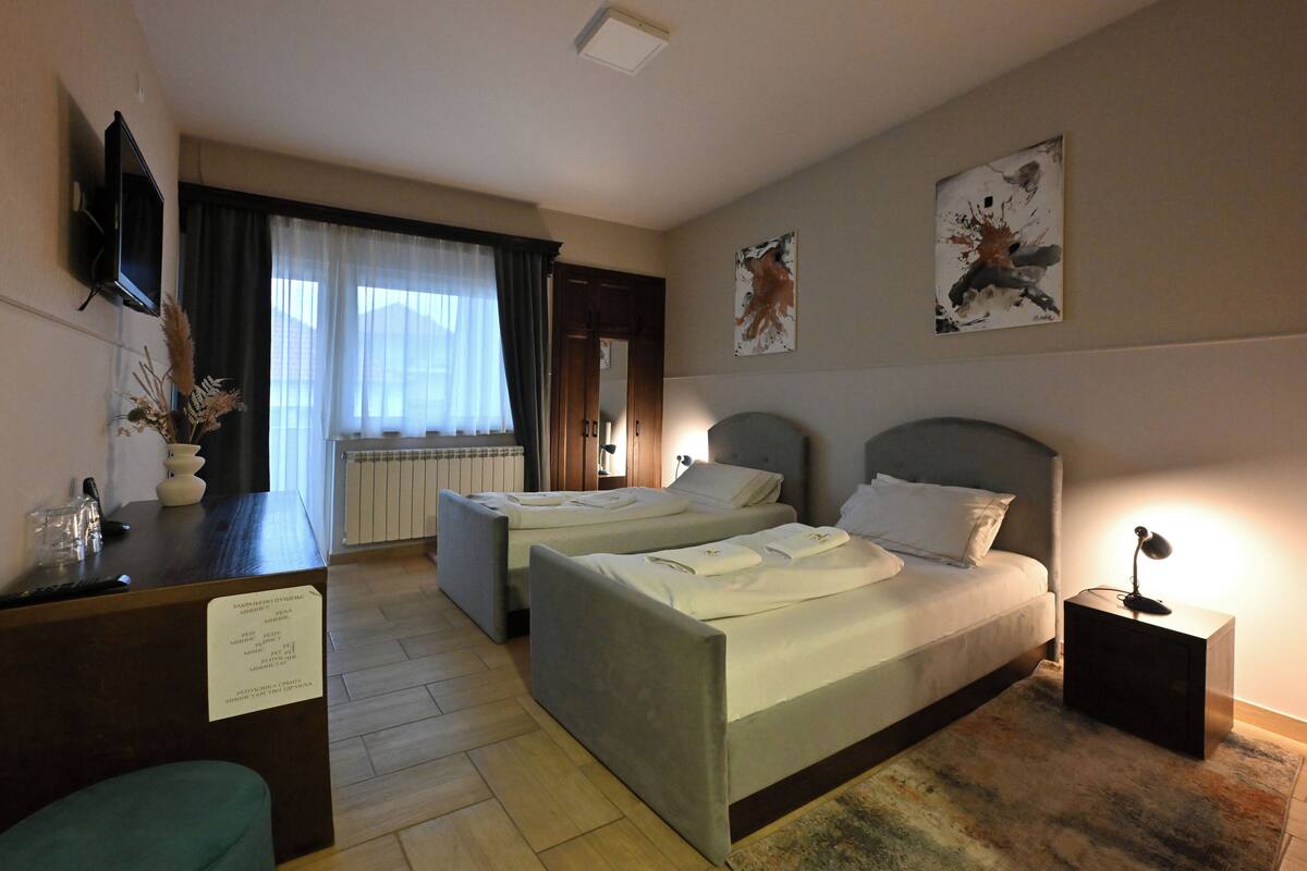 A hotel room with two beds, a desk, a TV, and artwork on the walls.