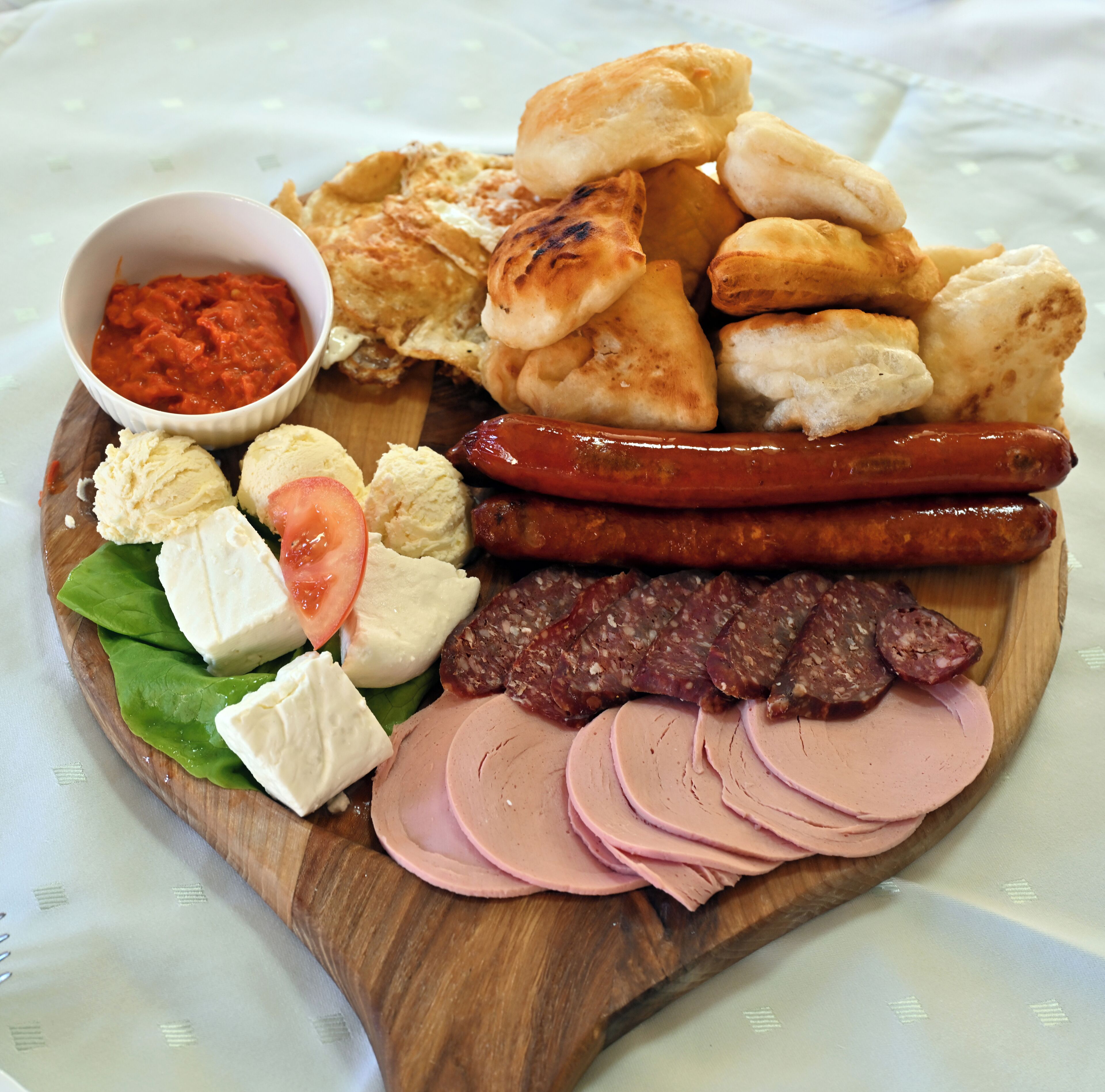 A wooden board with various food items including sausages, cheese, and bread.