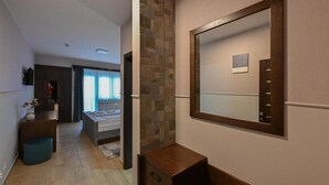 A modern bedroom with a large mirror, a stone accent wall, and a view of the adjacent room.