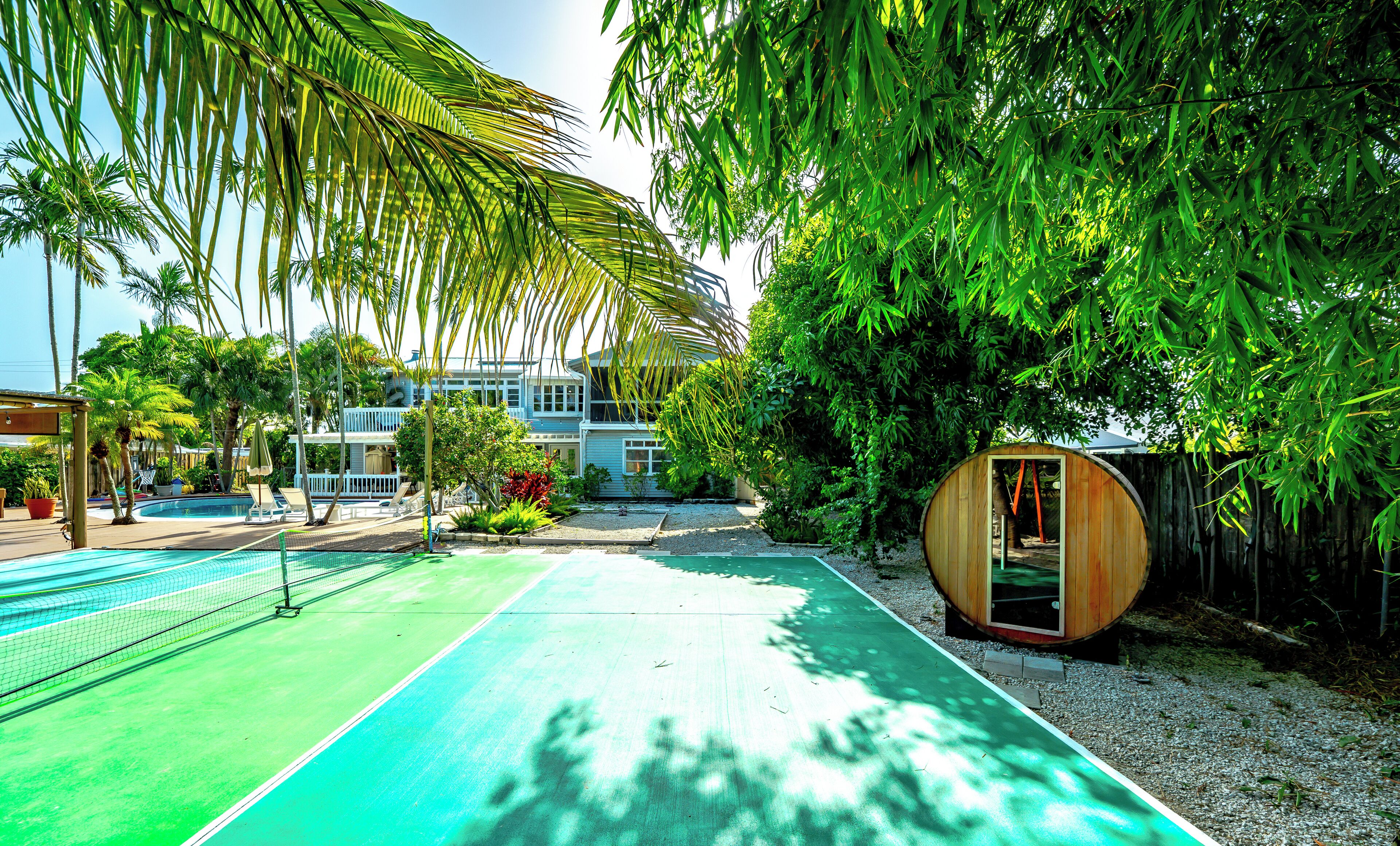 A tennis court with a net, surrounded by palm trees and a wooden structure.