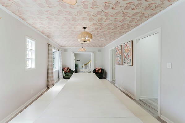 A hallway with patterned ceiling, a chandelier, and two green armchairs with floral cushions.
