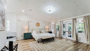 A bedroom with a bed, bedside tables, a bench, a wooden floor, a checkered rug, and a view of the outdoors through a door. - Serenity Stays (West Palm Beach)