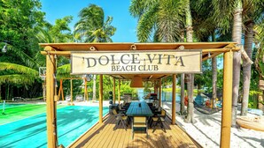 A wooden deck with a sign reading "DOLCE VITA BEACH CLUB" and a pool area. - Serenity Stays (West Palm Beach)