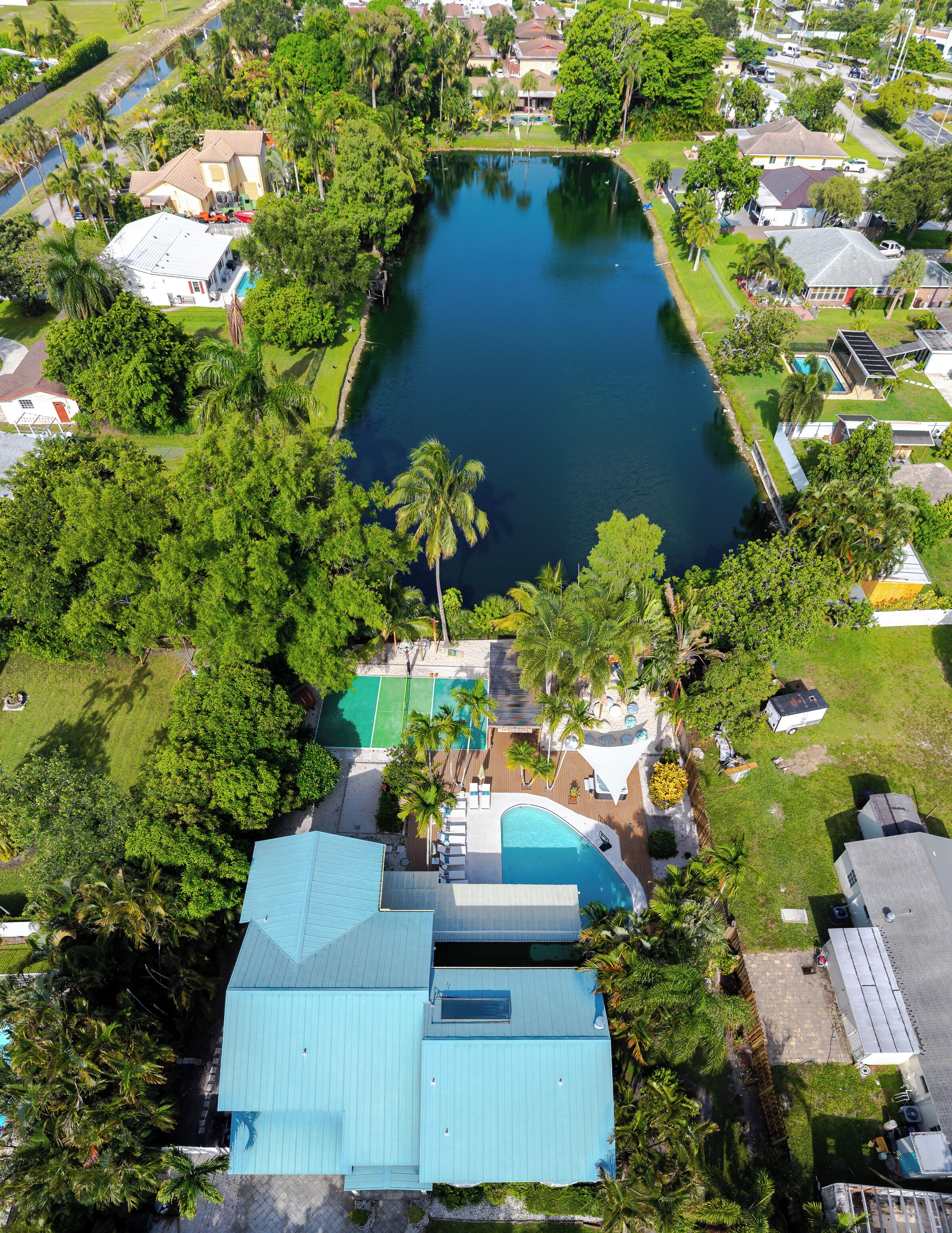 An aerial view of a residential area with a large pond, surrounded by lush greenery and houses.
