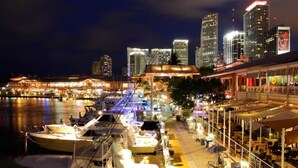 A waterfront marina with boats docked, a restaurant with outdoor seating, and a city skyline in the background. - Quiet Miami Stay•Perfect for Work,Relax, or party! (Miami)