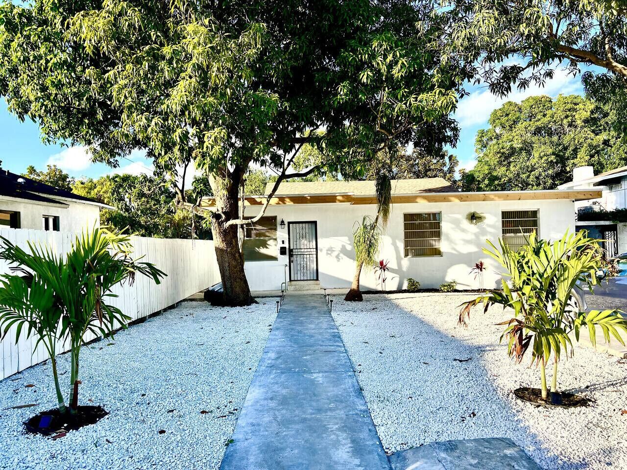 A pathway leading to a house with a white exterior, surrounded by gravel and small plants.