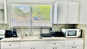 A kitchen with white cabinets, a microwave, a coffee maker, and a window with blinds. - Quiet Miami Stay•Perfect for Work,Relax, or party! (Miami)