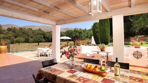 An outdoor patio with a table set for dining, surrounded by potted plants and a view of the countryside. - Villa Tirana (Pollença)