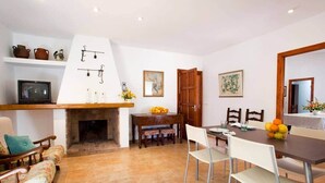 A dining area with a fireplace, a television, and a dining table with chairs. - Villa Tirana (Pollença)