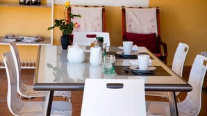 A dining table set with white teapots, cups, and saucers, surrounded by clear chairs. - Villa Tirana (Pollença)