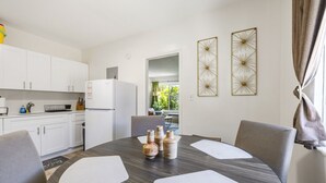 A modern kitchen with white cabinets, a white refrigerator, and a dining area with a round table and grey chairs. - Urban Oasis • Modern Comfort in Prime Location (Miami)