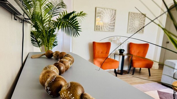 A modern interior with a long wooden decorative piece on a table, a potted plant, and orange chairs. - Urban Oasis • Modern Comfort in Prime Location (Miami)
