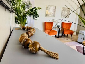 A modern interior with a long wooden decorative piece on a table, a potted plant, and orange chairs. - Urban Oasis • Modern Comfort in Prime Location (Miami)