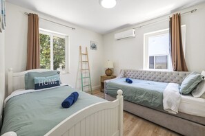 A bedroom with two beds, a ladder, an air conditioning unit, and a window with curtains.