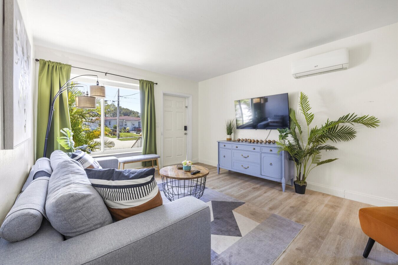 Ein Wohnzimmer mit einer Couch, einem Couchtisch, einem Fernseher, einem blauen Schrank und einer großen Pflanze.