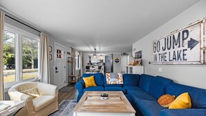 A modern living room with a blue sofa, a white armchair, and a coffee table. A sign on the wall reads "GO JUMP IN THE LAKE".
