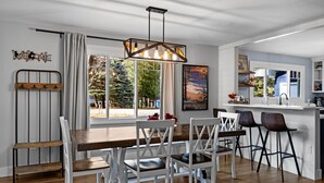 A modern dining area with a wooden table, white chairs, and a bar with stools.